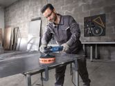 Một người mặc đồ bảo hộ đang đánh bóng tấm kim loại bằng dụng cụ điện.