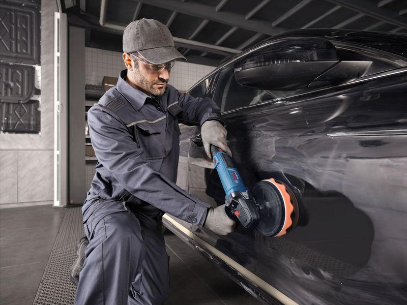 Một người mặc đồ bảo hộ đang đánh bóng một chiếc ô tô màu đen bằng dụng cụ điện.