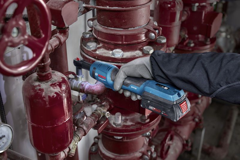 Một người mặc thiết bị an toàn đang sử dụng cờ lê không dây trên đường ống công nghiệp.