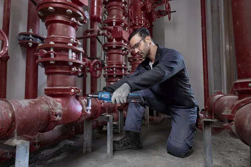 Một người mặc thiết bị an toàn đang sử dụng cờ lê không dây trên hệ thống ống màu đỏ.