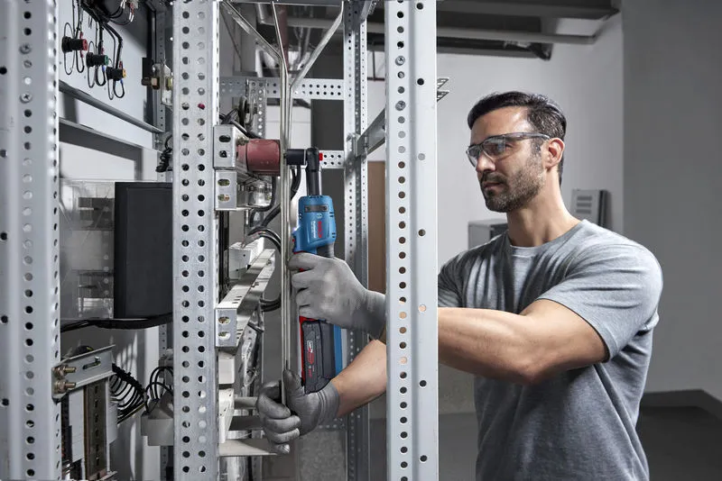 Một người mặc thiết bị an toàn đang sử dụng cờ lê không dây trên giá kim loại.