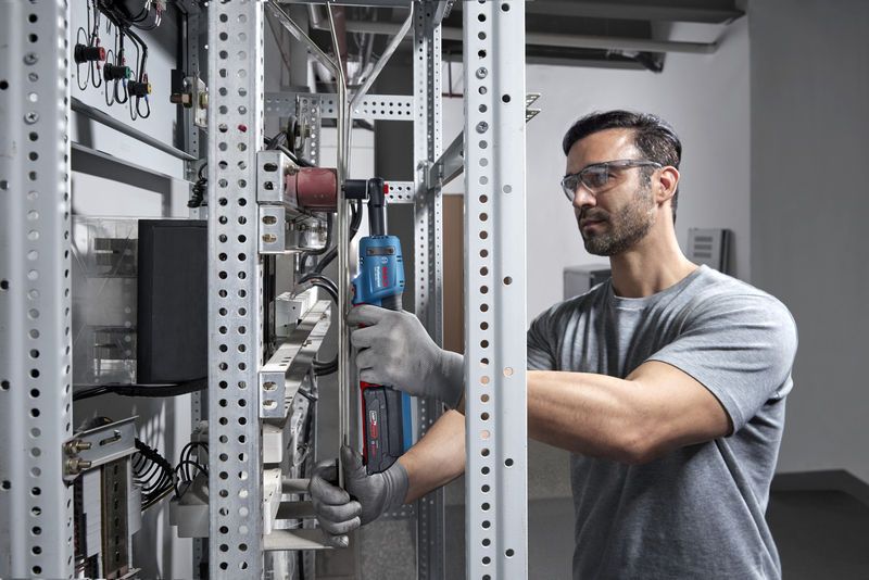 Một người mặc thiết bị an toàn đang sử dụng cờ lê không dây trên giá kim loại.