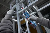 Một người mặc đồ bảo hộ đang siết chặt bu lông trên khung kim loại bằng cờ lê không dây.
