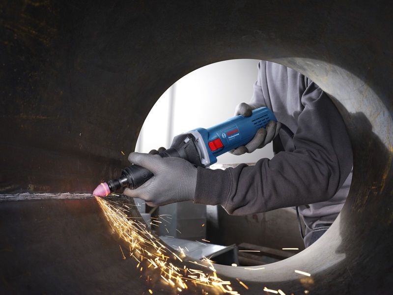 Một người mặc đồ bảo hộ sử dụng máy mài thẳng để làm phẳng bên trong ống kim loại.