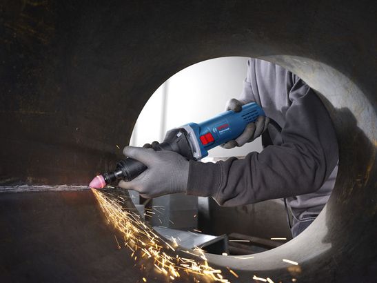 GGS 5 LS Một người mặc đồ bảo hộ đang mài bên trong một ống kim loại lớn bằng máy mài góc.