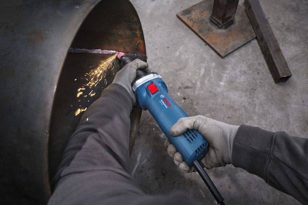 GGS 5 LS Một người đeo thiết bị an toàn đang mài cạnh của một ống kim loại lớn bằng một dụng cụ điện.