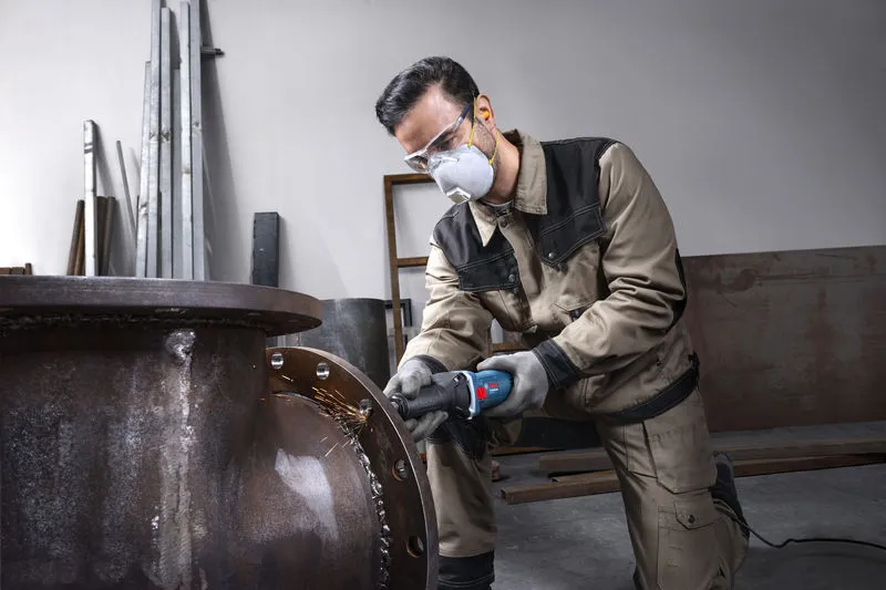 GGS 5 LS Một người mặc đồ bảo hộ đang mài mép của một ống kim loại lớn.