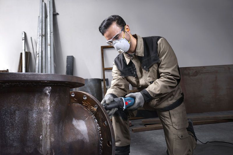 Một người mặc đồ bảo hộ đang mài mép của một ống kim loại lớn.