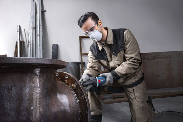GGS 5 LS Một người mặc thiết bị an toàn đang sử dụng máy mài góc để làm nhẵn một ống kim loại lớn.