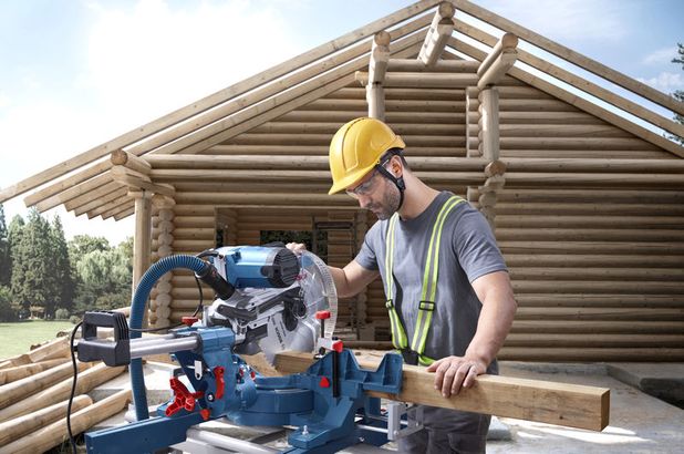 GCM 340-305 D Một người mặc đồ bảo hộ đang cắt gỗ bằng máy cưa góc tại công trường xây dựng nhà gỗ.