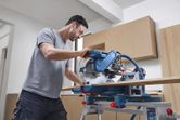 Một người mặc đồ bảo hộ đang cắt gỗ bằng máy cưa góc trong xưởng.
