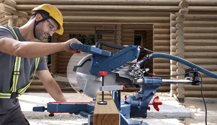 GCM 340-305 D Một người mặc đồ bảo hộ đang vận hành máy cưa góc để cắt gỗ tại công trường xây dựng.