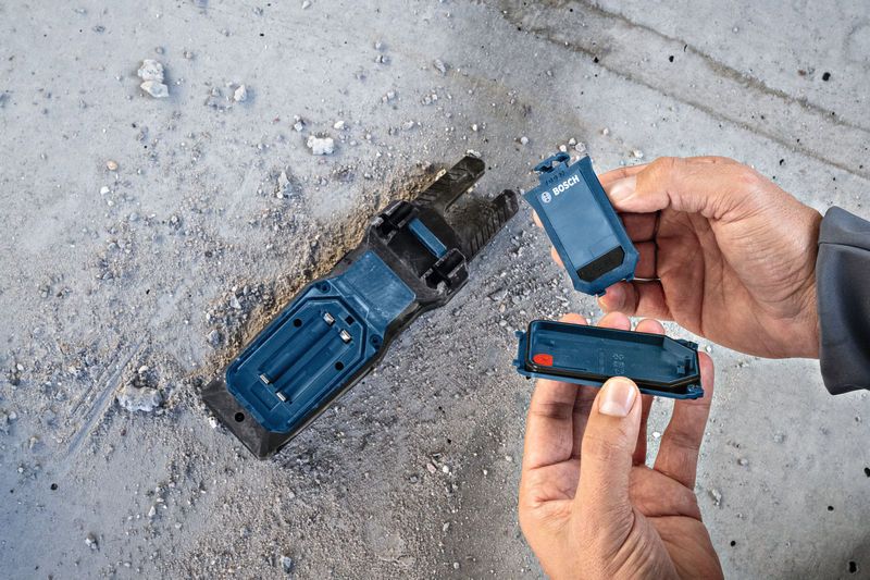 Người đang thay pin cho đế dụng cụ điện trên sàn bê tông bụi bặm.