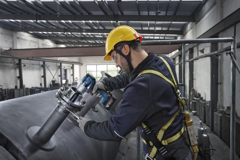 Một người mặc thiết bị an toàn sử dụng cờ lê tác động để siết chặt bu lông trên một bể kim loại lớn.