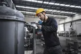 Một người mặc thiết bị an toàn đang sử dụng cờ lê tác động không dây trên một ống kim loại lớn.