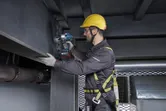 Một người mặc đồ bảo hộ đang siết chặt bu lông trên thanh thép bằng cờ lê lực không dây.