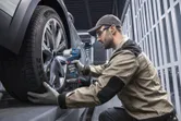 Một người mặc thiết bị an toàn sử dụng cờ lê lực không dây để siết chặt bánh xe ô tô.