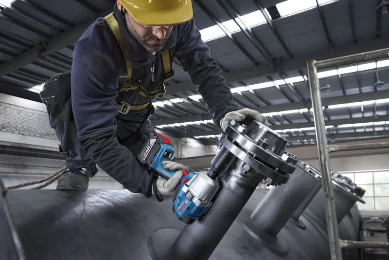 Một người mặc đồ bảo hộ đang sử dụng cờ lê lực không dây trên đường ống công nghiệp.