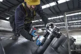 Một người mặc đồ bảo hộ đang sử dụng cờ lê lực không dây trên đường ống công nghiệp.