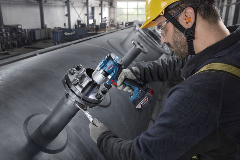 Một người mặc đồ bảo hộ đang siết chặt bu lông trên đường ống công nghiệp bằng cờ lê lực không dây.