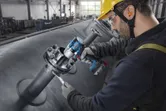 Một người mặc đồ bảo hộ đang siết chặt bu lông trên đường ống công nghiệp bằng cờ lê lực không dây.
