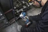 Một người mặc đồ bảo hộ đang siết chặt bu lông trên máy móc công nghiệp bằng cờ lê lực không dây.