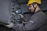 Một người mặc thiết bị an toàn đang sử dụng cờ lê tác động không dây trên một thanh thép.
