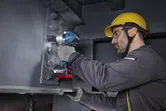 Một người mặc đồ bảo hộ đang siết chặt bu lông trên thanh thép bằng cờ lê lực không dây.