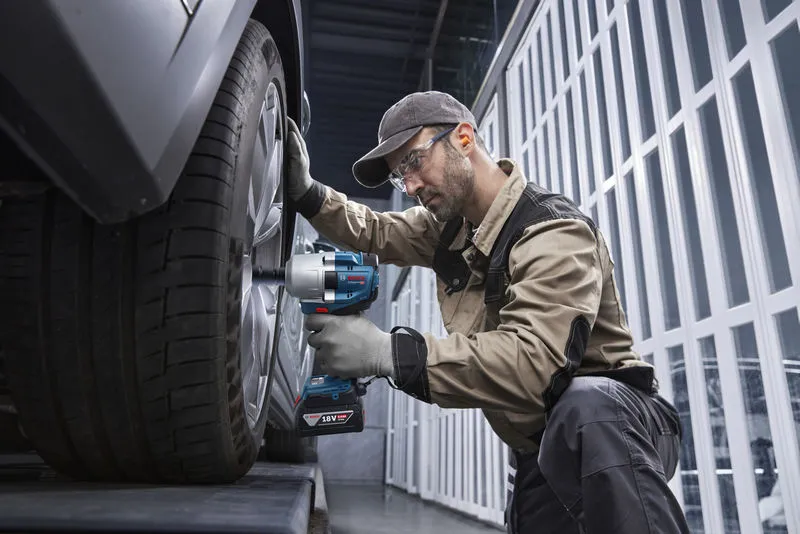 Một người mặc thiết bị an toàn đang sử dụng cờ lê tác động không dây để tháo bánh xe ô tô.