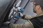 Một người mặc thiết bị an toàn đang sử dụng cờ lê tác động không dây để tháo bánh xe ô tô.