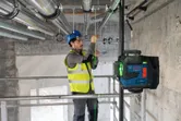 Một người mặc thiết bị an toàn đang căn chỉnh các đường ống bằng dụng cụ cân bằng laser.