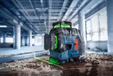 Máy cân bằng laser chiếu những đường màu xanh lá cây trên sàn bụi tại một công trường xây dựng.