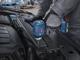 Một người mặc thiết bị an toàn sử dụng máy vặn vít để vặn chặt một con ốc trong khoang động cơ ô tô.