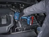 Một người mặc thiết bị an toàn đang sử dụng máy siết bu lông không dây vào động cơ ô tô.