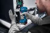 Một người mặc thiết bị an toàn sử dụng máy vặn vít không dây để lắp ráp thiết bị điện tử.