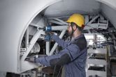 Một người mặc thiết bị an toàn sử dụng cờ lê tác động vào khung kim loại.