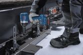 Một người mặc thiết bị an toàn sử dụng cờ lê tác động để vặn chặt bu lông trên khung kim loại.