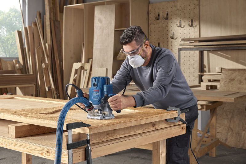 Một người mặc đồ bảo hộ đang sử dụng máy phay để định hình gỗ trong xưởng.