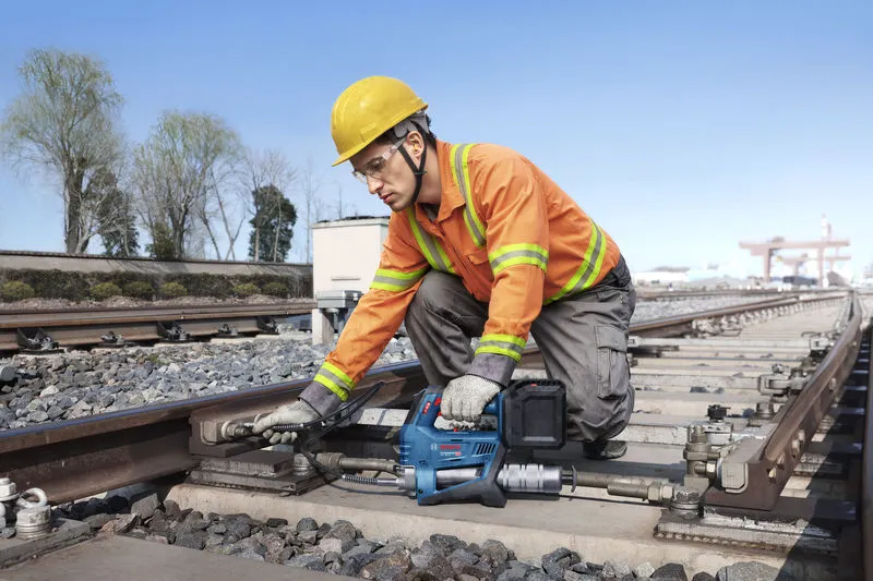 Một người mặc thiết bị an toàn sử dụng súng bơm mỡ không dây để bảo trì đường ray xe lửa.