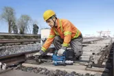 Một người mặc đồ bảo hộ đang sử dụng dụng cụ điện để bảo trì đường ray xe lửa.