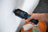 Một người sử dụng máy đo độ ẩm vật liệu để kiểm tra một bức tường màu trắng.