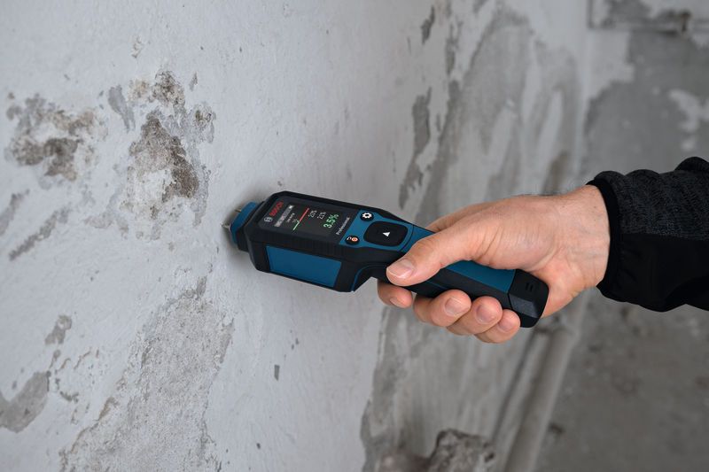 Một người sử dụng máy đo độ ẩm vật liệu để kiểm tra bức tường bê tông.