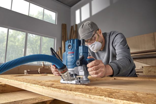 GOF 20-12 Một người mặc đồ bảo hộ đang sử dụng máy phay trên tấm ván gỗ trong xưởng.