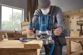 Một người mặc đồ bảo hộ sử dụng máy phay để định hình cạnh của một tấm ván gỗ.
