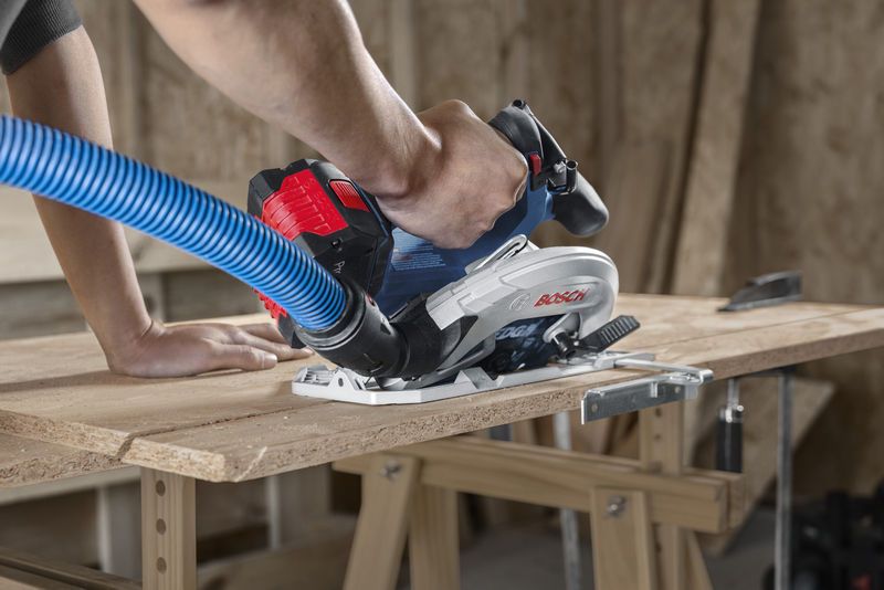 Một người đang điều khiển máy cưa tròn không dây có ống hút bụi trong khi cắt ván ép.