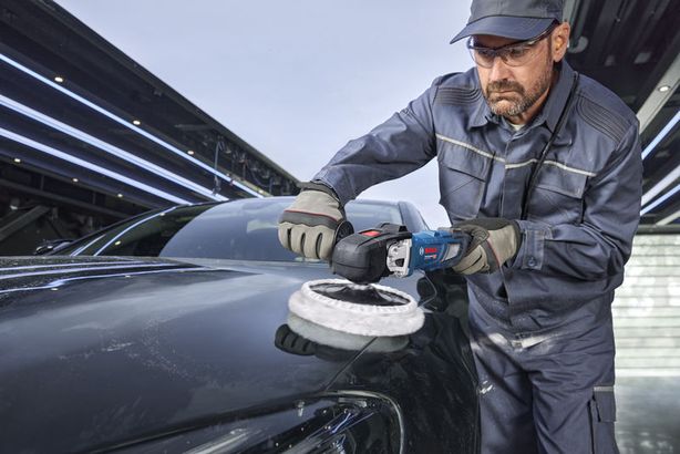 GPO 14-180 S Một người mặc đồ bảo hộ đang đánh bóng mui xe ô tô màu đen bằng máy đánh bóng điện.