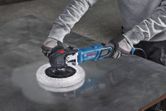 Một người mặc đồ bảo hộ đang đánh bóng tấm kim loại bằng máy đánh bóng điện.