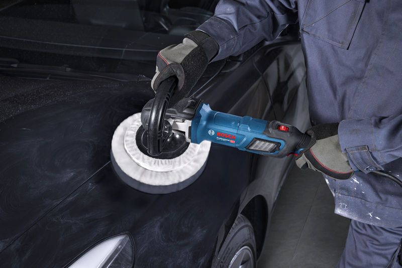 Một người mặc đồ bảo hộ đang sử dụng máy đánh bóng trên mui xe màu đen.