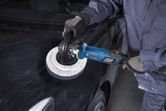 Một người mặc đồ bảo hộ đang sử dụng máy đánh bóng trên mui xe màu đen.