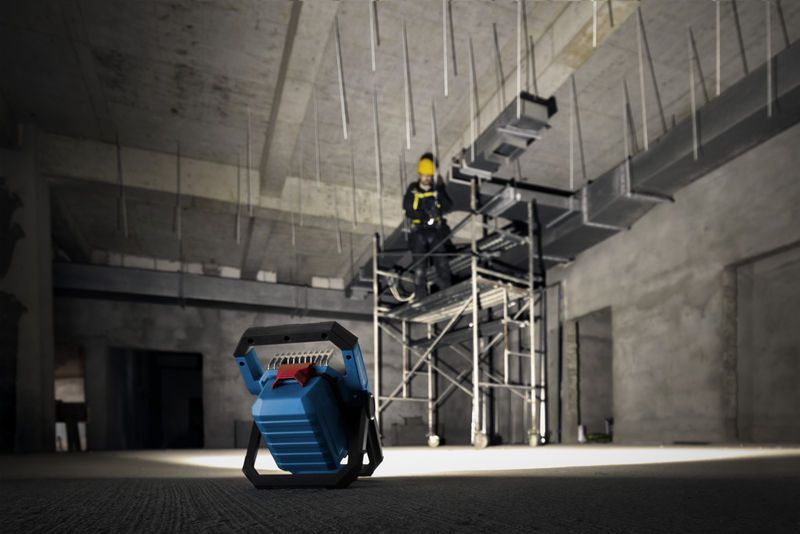 Đèn công trường không dây chiếu sáng cho người đang mặc đồ bảo hộ trên giàn giáo.